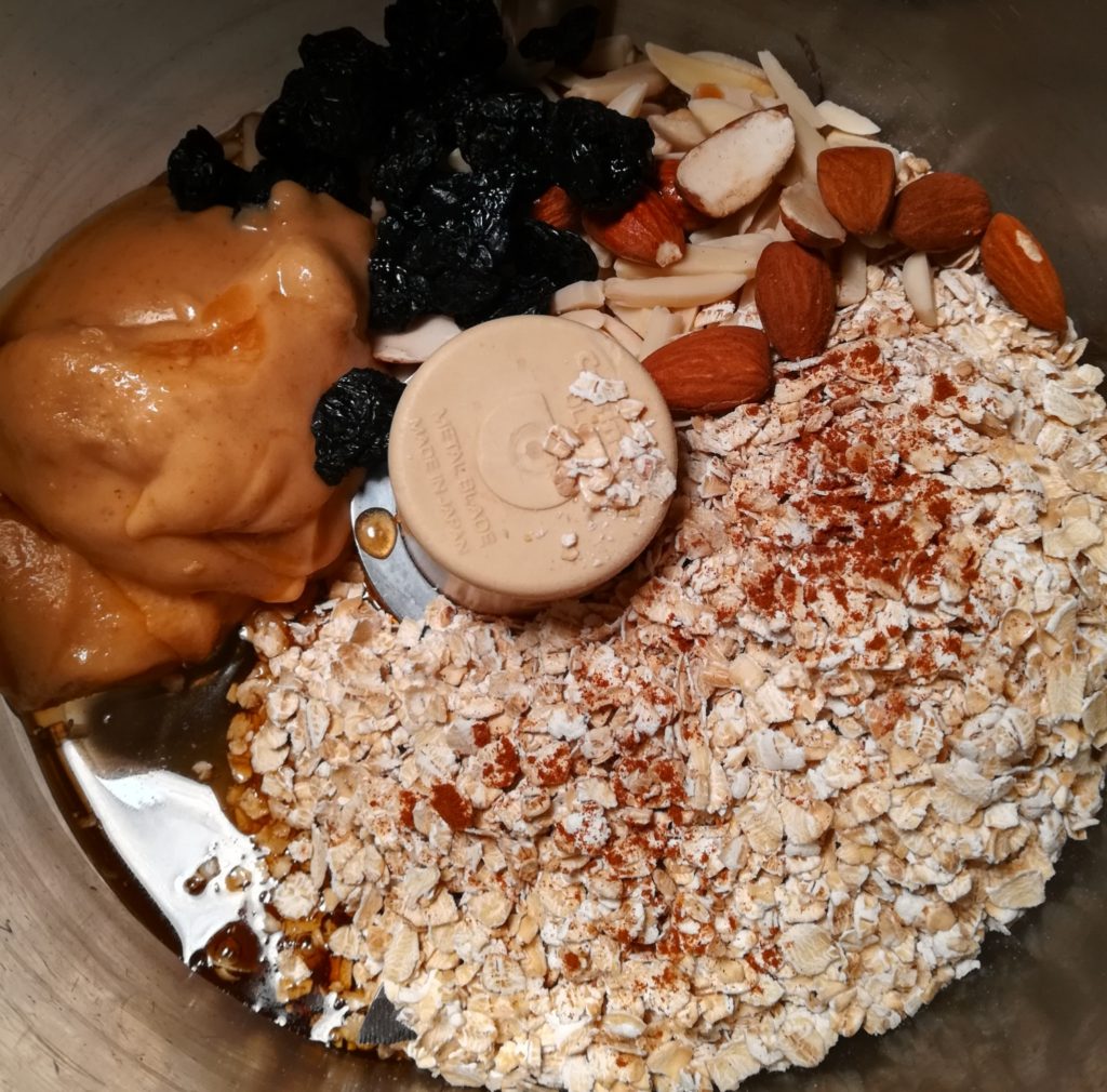 Mixing oats, nut butter, dried cherries, and almonds in a food processor