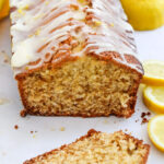 Lemon loaf cake with glaze shown on a tabletop with fresh lemon slices